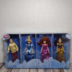 three disney princess dolls in their packaging on a wooden table with white wall behind them