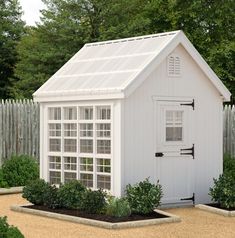 a small white shed with windows on the side and plants growing in the front yard