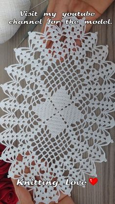 someone is crocheting a white doily with red roses on the table next to it