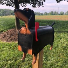 a dog shaped mailbox sitting on top of a wooden post next to a tree