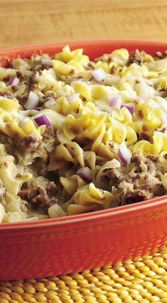 a red casserole dish filled with macaroni and cheese, meat and onions