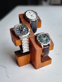 three watches sitting on top of each other on wooden stand with white marble countertop