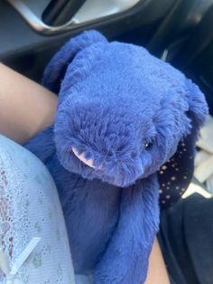 a blue teddy bear sitting in the driver's seat of a car with someone holding it