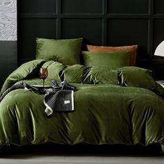 a bed with green sheets and pillows on top of it in front of a black wall