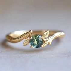 a gold ring with a green stone and leaves on the band, sitting on a white surface