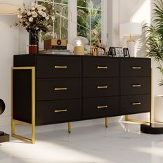 a black and gold dresser in a white room with plants on the side table next to it