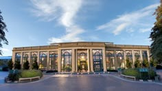 a large building with many windows and trees around it's entrance area at dusk