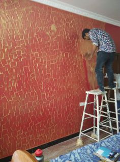 a man on a ladder painting a wall with red and gold paint in a bedroom