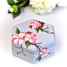 a small box with flowers painted on it next to some white and pink flowers in the background