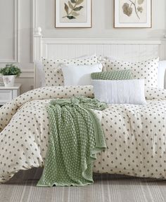 a bed with white and green comforters in a room next to two pictures on the wall