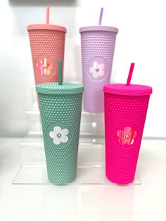 four different colored cups with straws in them on a white counter top and one has a flower design on the lid