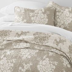 the comforter is made up with white and beige flowers on it's bed