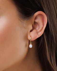 a woman wearing a pair of gold earrings with white pearls on the end of each ear