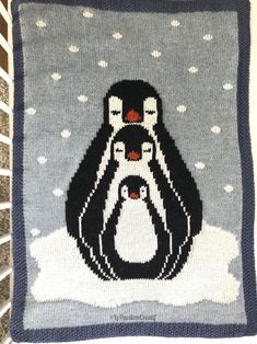 a crocheted blanket with two penguins on it and snowflakes in the background