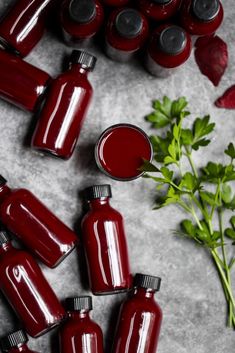 several red glass bottles are lined up next to some green leaves and flowers on a gray surface