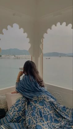 a woman sitting on top of a bed in front of a large body of water