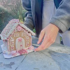 a person is decorating a gingerbread house with icing and pink sprinkles