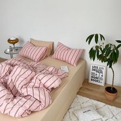 a bed with pink and white striped sheets on it next to a potted plant