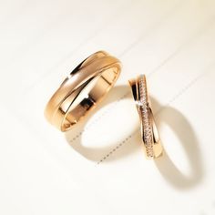 two gold wedding rings sitting on top of a white table next to an empty piece of paper