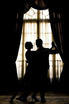 two people standing in front of a window with sheer drapes on the windowsill