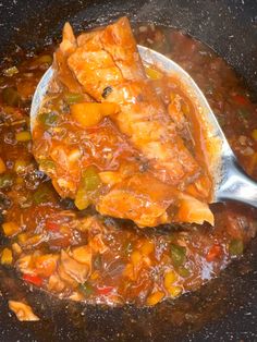 a spoon full of stew in a pot with meat and vegetables on the side,