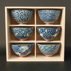 six blue and white bowls sitting in a wooden box on top of a black surface