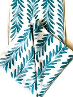 two napkins with blue leaves on them sitting next to each other in front of a white background