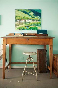 a painting is hanging on the wall above a desk with a chair and stool in front of it