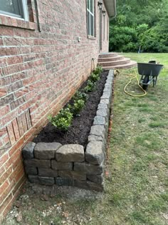 a brick wall with plants growing out of it next to a wheelbarrow in the grass