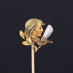 During the turn of the nineteenth century, artisans working in the Art Nouveau style were inspired by the changing roles of women in society and began depicting the free flowing feminine form in brooches, bracelets, rings and more. This antique stick pin (circa 1910-1920) features a woman of 14k gold decked out in enamel and accented with a single pearl. The piece bears the makers mark for the renowned Krementz and Co. The pin head measures 0.6 inches by 0.6 inches and 2.4 inches long. The piece Yellow Gold Enamel Brooches, Art Nouveau Yellow Gold Brooch Jewelry, Art Nouveau Yellow Gold Brooch, Artistic Enamel Jewelry For Formal Occasions, Victorian Style Enamel Pin Gift, Gold Formal Enamel Pin, Art Nouveau Gold Brooch With Cabochon, Art Nouveau Yellow Gold Collectible Brooches, Gold Art Nouveau Brooch For Collectors