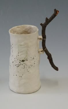 a white ceramic cup with a branch sticking out of it's side, on a gray background