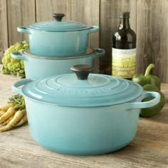 three blue casserole dishes sitting on top of a wooden table next to bottles of wine