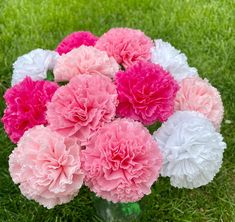 pink and white carnations are in a vase on the grass with green grass behind them