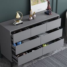 a grey dresser with drawers in front of a green wall and a painting on the wall