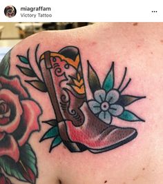 a tattoo on the back of a man's shoulder with flowers and an old boot