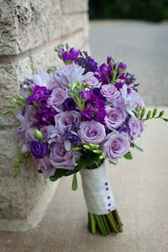 a bouquet of purple flowers sitting next to a stone wall