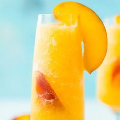 two glasses filled with orange juice on top of a table next to sliced peaches