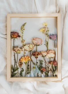 an arrangement of dried flowers in a wooden frame on a white bed linens background