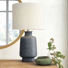 a table with a lamp, vase and mirror on it