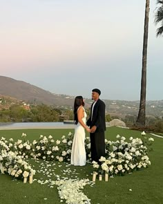 a newly married couple standing in front of a circular flower arrangement with white flowers on the grass