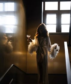 a woman in a robe holding a glass of wine and standing on the stairs with her hands behind her back