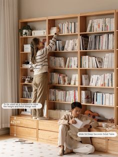 a woman standing on top of a book shelf next to a man sitting in front of a bookshelf