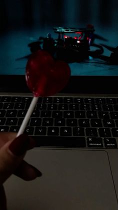 a person holding a lollipop in front of a laptop computer with the screen lit up