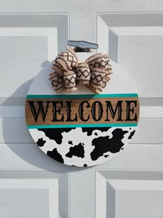 a welcome sign hanging on the side of a white door with black and brown cow prints