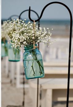 some flowers are in mason jars hanging from a pole on the beach, and one is filled with baby's breath