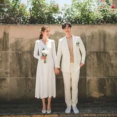 a man and woman standing next to each other in front of a wall with flowers on it