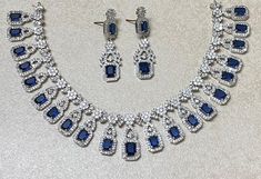 Sapphire Diamond Necklace Set features a stunning blue stone centerpiece surrounded by sparkling CZ American diamonds. The set includes a matching ring, making it a perfect statement piece for a contemporary Indian bride. Ideal as a wedding gift, it exudes elegance and modern sophistication. *𝐏𝐑𝐎𝐃𝐔𝐂𝐓 𝐃𝐄𝐓𝐀𝐈𝐋* * 𝐌𝐚𝐭𝐞𝐫𝐢𝐚𝐥: Brass * 𝐏𝐥𝐚𝐭𝐢𝐧𝐠: White Rhodium Plated * 𝐒𝐭𝐨𝐧𝐞: AAA-quality CZ Diamond & Sapphire. *𝐃𝐈𝐌𝐄𝐍𝐒𝐈𝐎𝐍𝐒* *𝐍𝐞𝐜𝐤𝐥𝐚𝐜𝐞* * 𝐖𝐞𝐢𝐠𝐡𝐭: 56 gm Sapphire Cubic Zirconia Jewelry Set For Party, Wedding Jewelry With Sapphire And Diamond Accents, Blue Hand Set Jewelry For Party, Blue Rhinestone Jewelry For Gifts, Blue Cubic Zirconia Necklace For Party, Elegant Sapphire Bridal Necklace In Cubic Zirconia, Elegant Bridal Necklace With Sapphire Cubic Zirconia, Blue Round Jewelry Sets For Wedding, Dazzling Sapphire Jewelry For Wedding