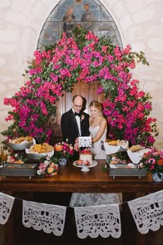 a bride and groom standing in front of a table with food on it, surrounded by flowers