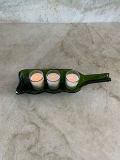 three lit candles sit in a green bottle on a marble counter top, with the lid partially open