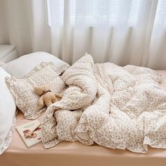 an unmade bed with a teddy bear on it next to pillows and a book